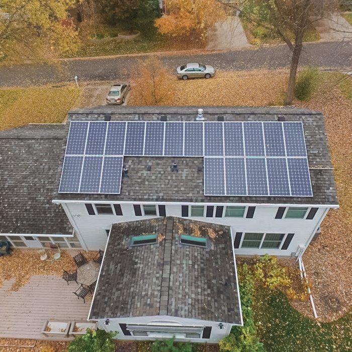 Aerial view of a solar farm with trees and a barn in the background - Solar Systems For Homes