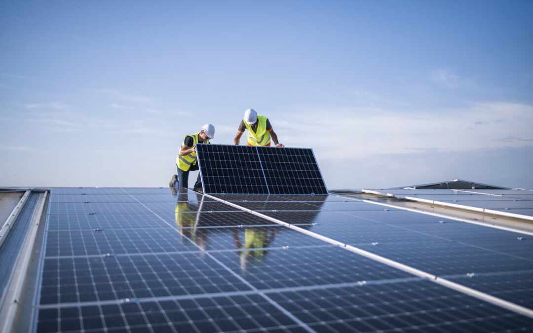 two men in yellow vests standing on top of a solar panel - Cedar Creek Energy