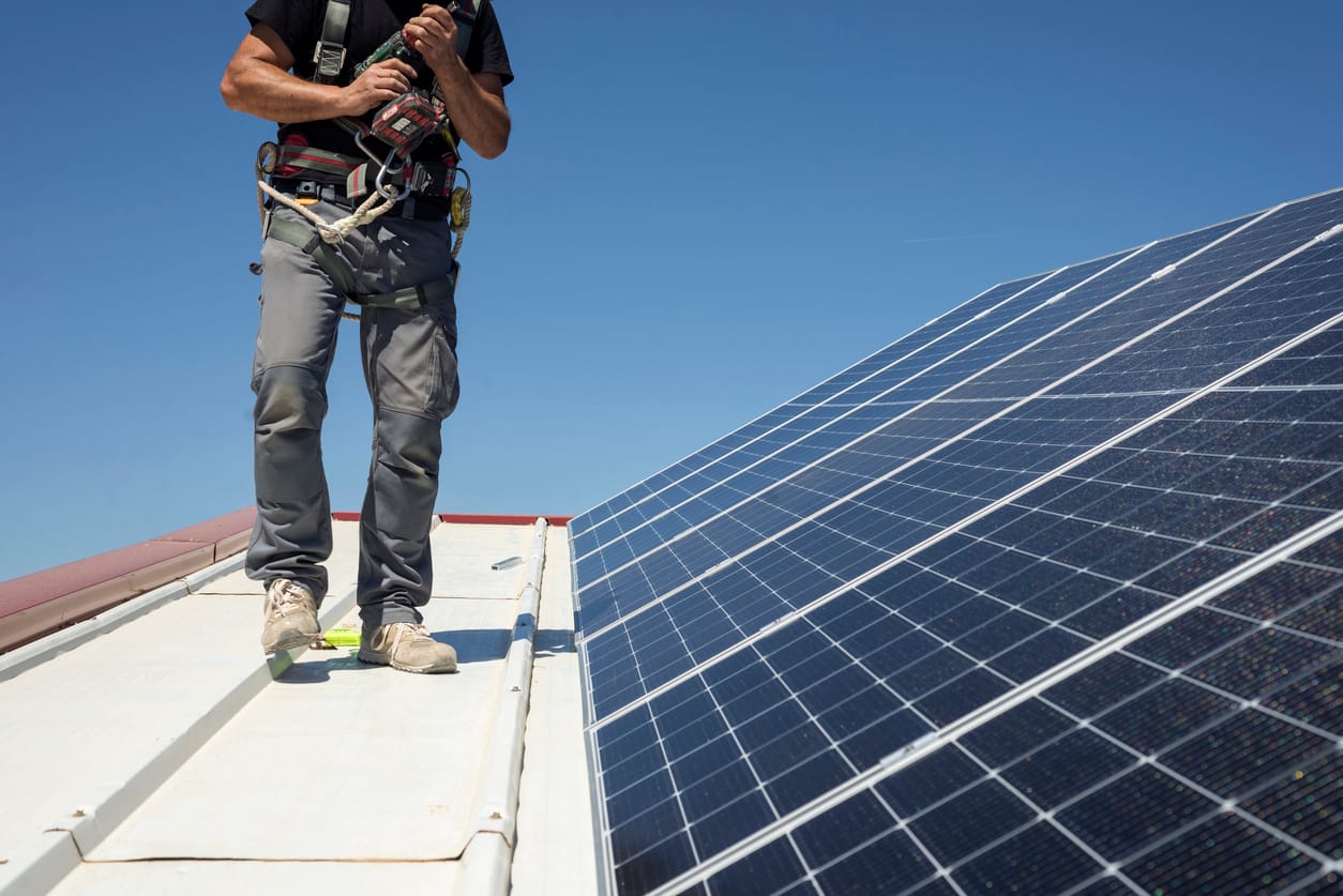 a man standing on top of a roof next to a solar panel - Solar Installation Process
